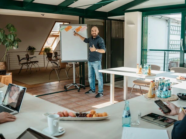 LifestyleWerkstatt - Workshop-Raum Gemütlicher Workshop-Raum mit eingedeckten Tischen, ein Mann präsentiert am Flipchart.