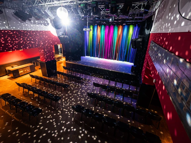 Bahnhof Langendreer Bochum Nachweis Christoph Partsch_4.jpg Bühnenraum mit buntem Vorhang, Stuhlreihen und Lichtpunkten einer Disco-Kugel