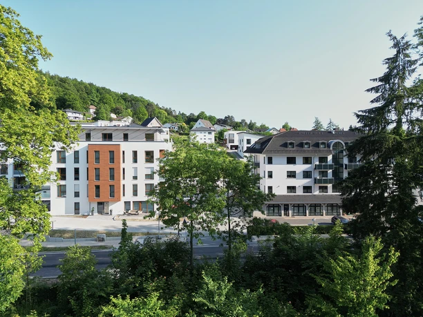 Premium Penthouse Parkblick Moderne Wohngebäude hinter Baumreihen vor bewaldetem Hang in Bad Driburg.