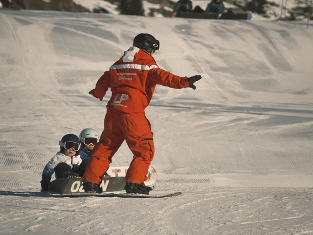 Snowboardunterricht für Kinder auf der Bettmeralp Die Skischule unterstützt Kinder beim Snowboard Schnupperkurs Bettmeralp auf einer flachen Übungspiste