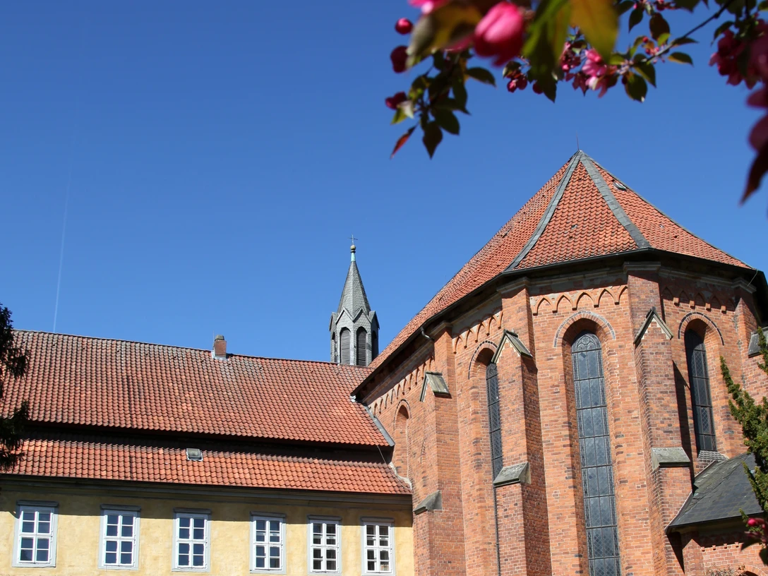 Kloster Mariensee Backsteinbau des Klosters Mariensee mit gelbem Konventgebäude, Garten und blühenden Zweigen im Vordergrund.