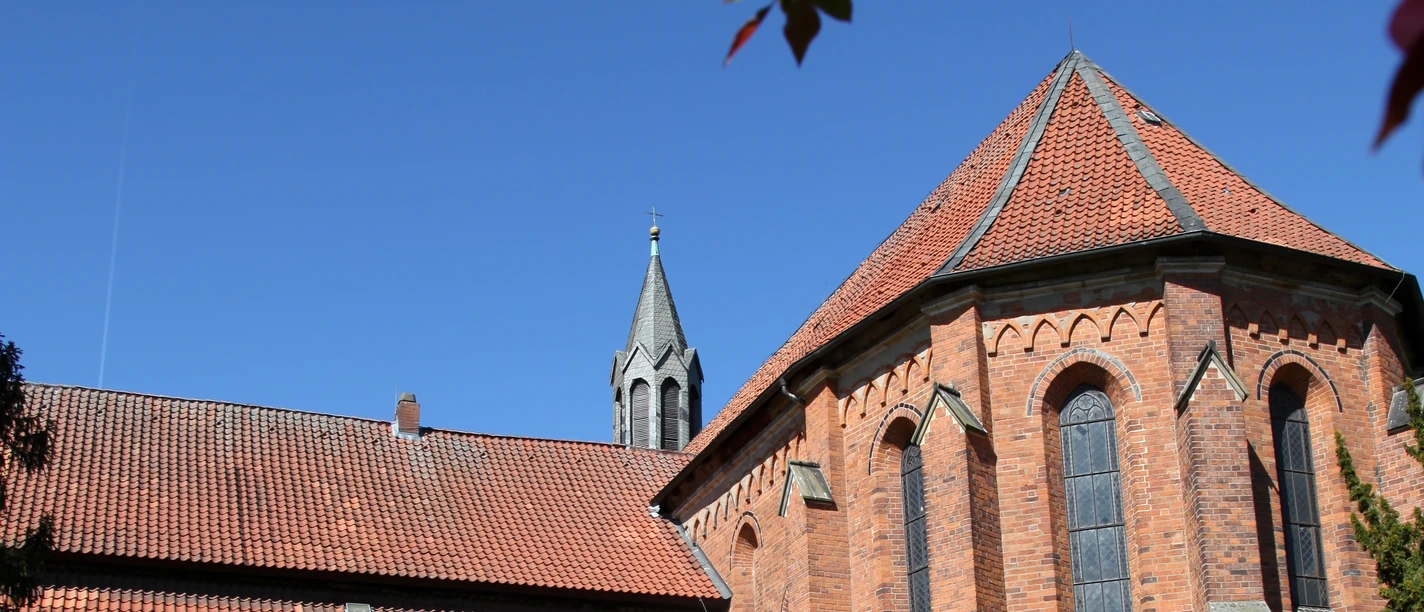 Kloster Mariensee Backsteinbau des Klosters Mariensee mit gelbem Konventgebäude, Garten und blühenden Zweigen im Vordergrund.