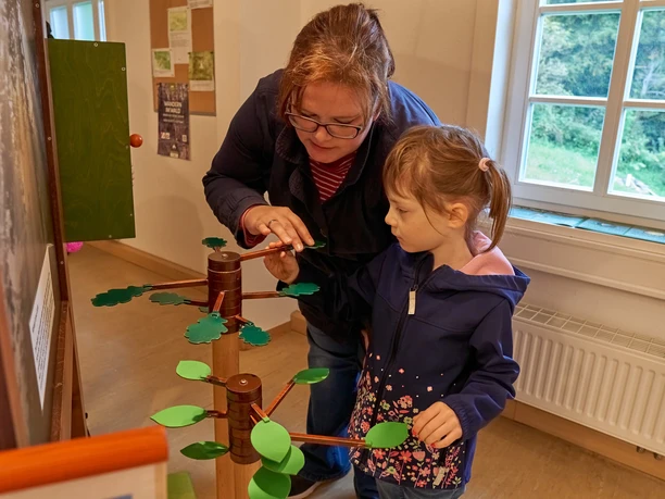 Frau und Mädchen spielen mit einem Holzbaumspiel in einem Raum.