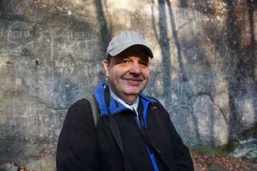 Mann mit Kappe und Rucksack lächelt vor Felswand.