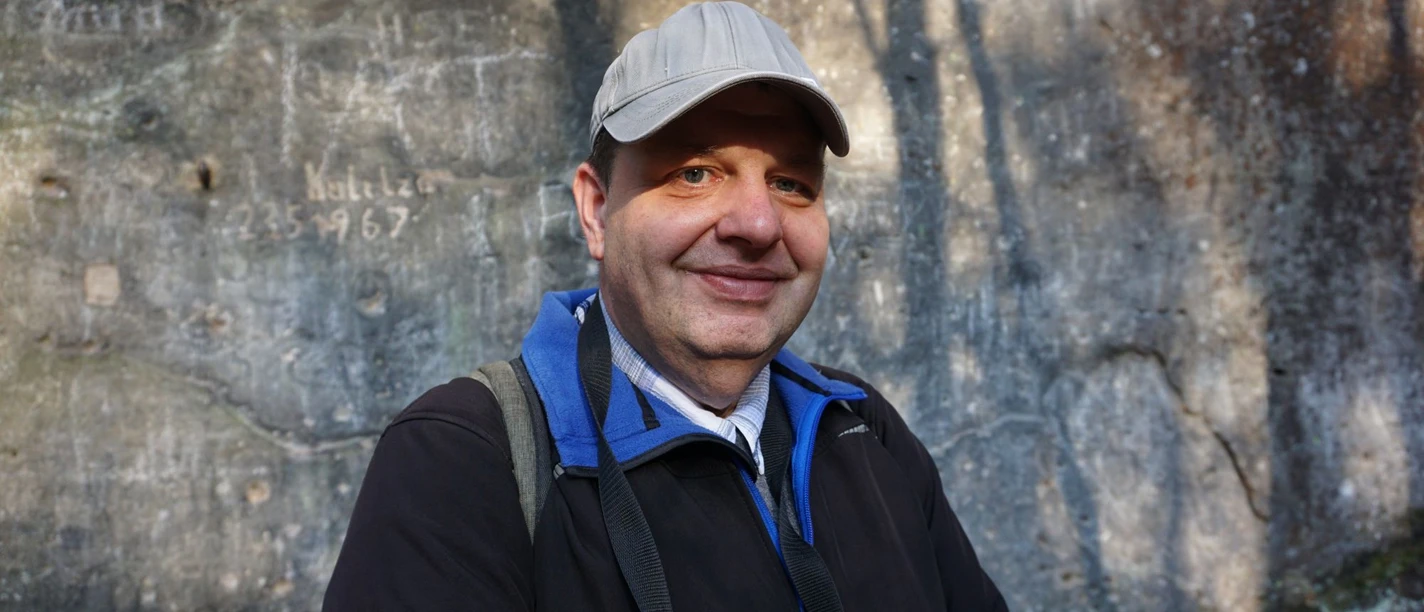 Mann mit Kappe und Rucksack lächelt vor Felswand.