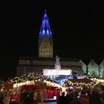 Weihnachtsmarkt bei Nacht: Menschen vor beleuchtetem Stand, beleuchteter Turm im Hintergrund.