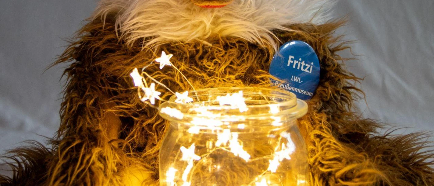 Auf dem Bild ist das Plüschtier Fritzi zu sehen - vor ihm steht ein Glas mit einer leuchtenden Lichterkette.
