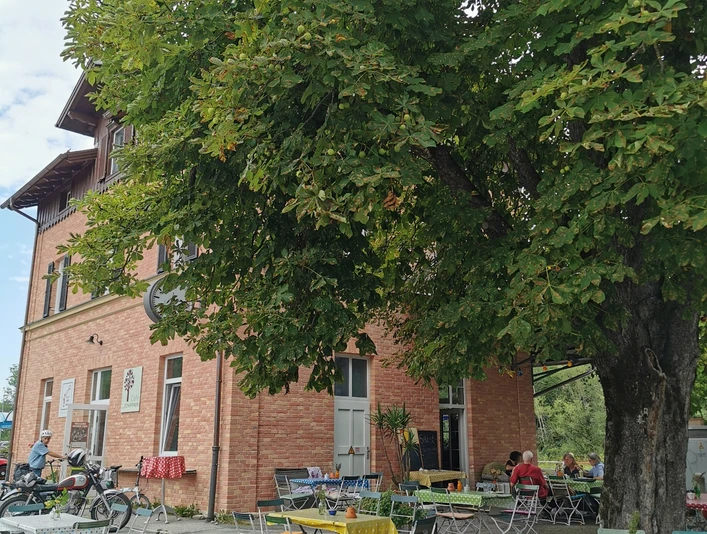 Café Schaffner Großer Baum mit Tischen vor rotem Haus. Gäste genießen Pausen im Freien.