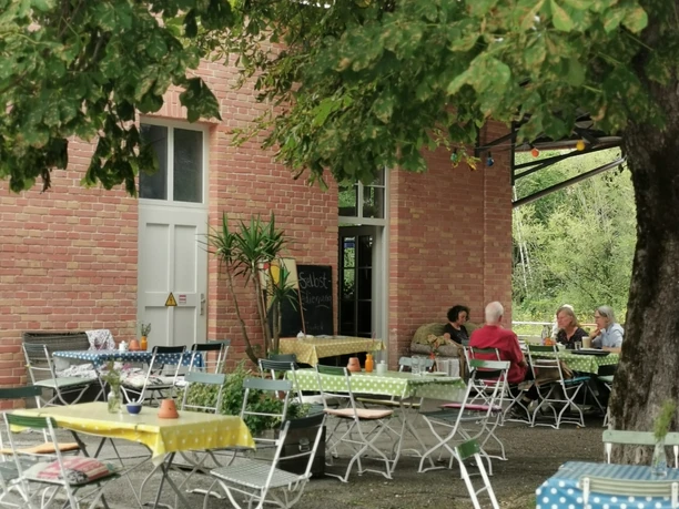 Café Schaffner Außenbereich eines Cafés mit bunten Tischen unter großem Baum und Menschen beim Kaffee.