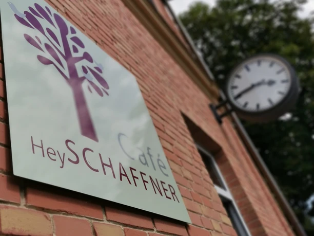Café Schaffner Ein einladendes Schild vom Café Hey Schaffner hängt an Ziegeln. Daneben eine Uhr.