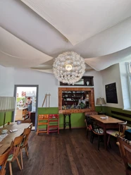 Café Schaffner Heller Raum mit Tischen und großer Lampe. Ein offener Tresen zeigt ein Café.