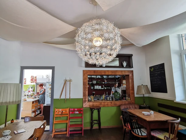 Café Schaffner Heller Raum mit Tischen und großer Lampe. Ein offener Tresen zeigt ein Café.