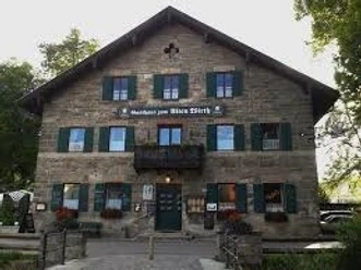 Zum alten Wirth Ein großes Gasthaus aus Stein steht vor Bäumen und zeigt grüne Fensterläden.
