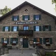 Zum alten Wirth Ein großes Gasthaus aus Stein steht vor Bäumen und zeigt grüne Fensterläden.