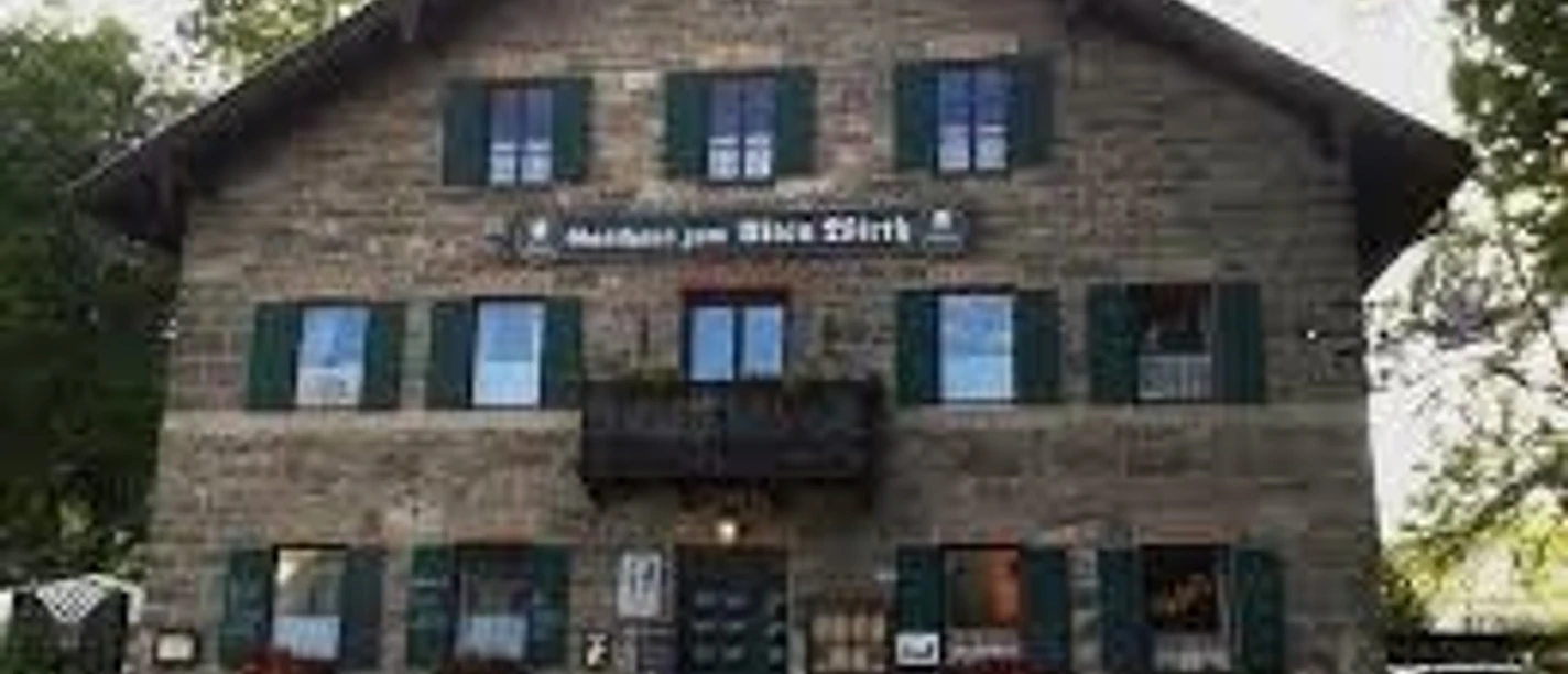 Zum alten Wirth Ein großes Gasthaus aus Stein steht vor Bäumen und zeigt grüne Fensterläden.