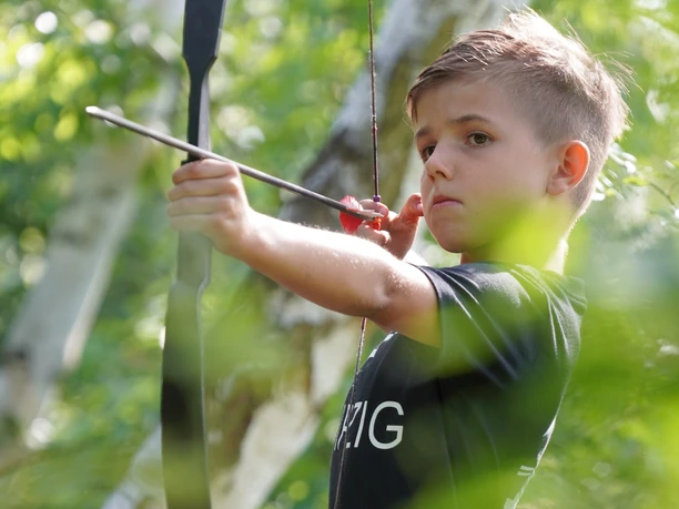 Un petit garçon s'entraîne au tir à l'arc, tient son arc avec concentration dans ses mains et vise avec attention.