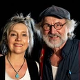 Klaus-Peter Wolf und Bettina Goeschl Zwei Erwachsene stehen nah beieinander vor dunklem Hintergrund und lächeln in die Kamera