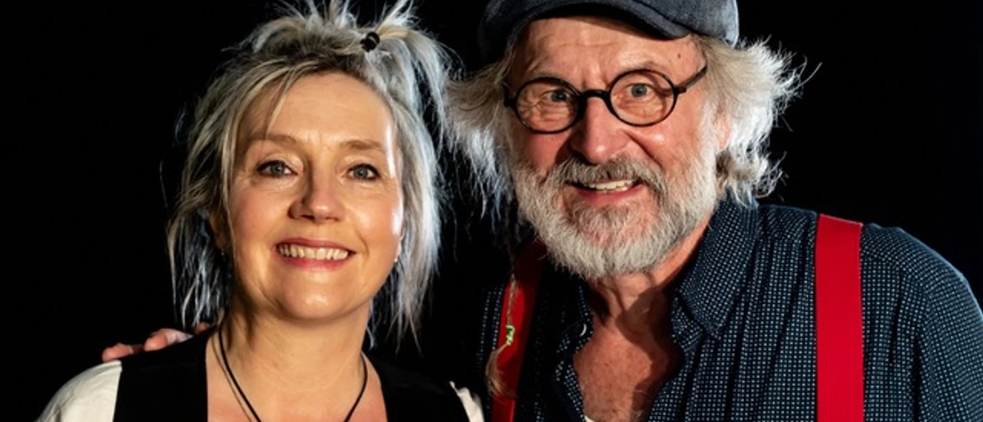 Klaus-Peter Wolf und Bettina Goeschl Zwei Erwachsene stehen nah beieinander vor dunklem Hintergrund und lächeln in die Kamera