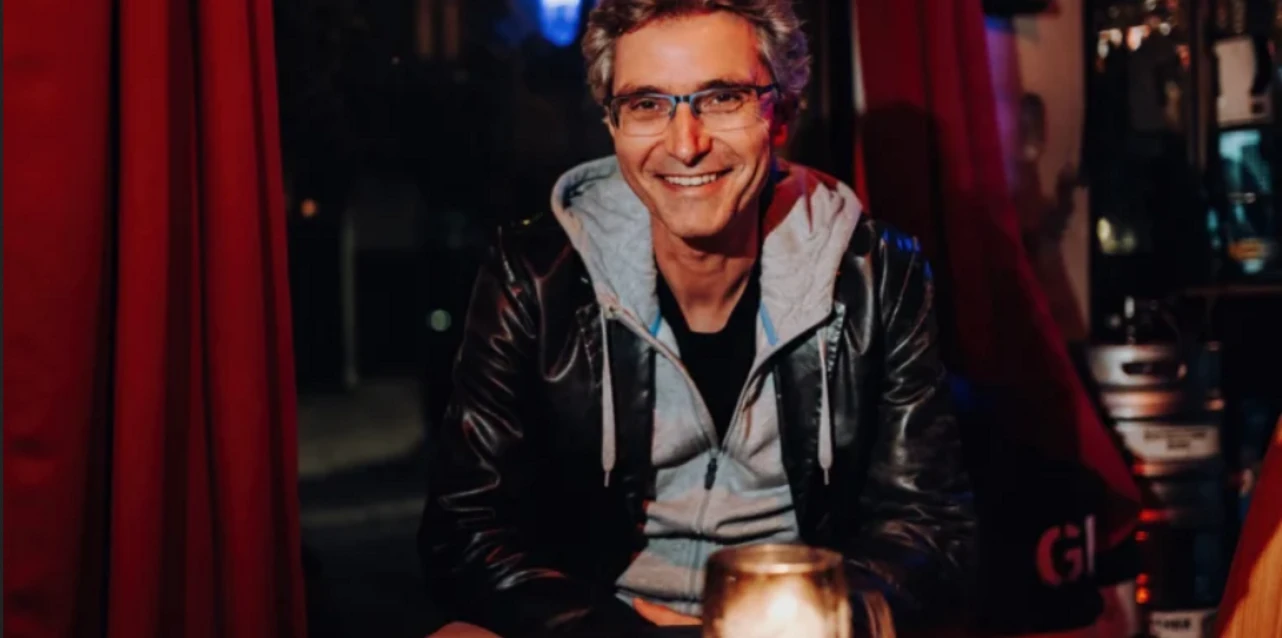 Mark Daniel Mann mit Brille lächelt in dunkler Bar an Tisch mit Kerzenlicht.