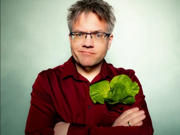 Pressefoto Matthias Reuter Person mit rotem Hemd und Salatblatt in der Brusttasche vor grünem Hintergrund.