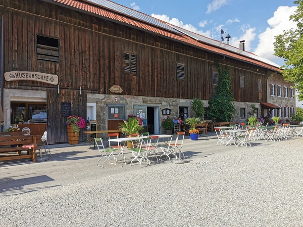 Museumcafe Vor einem alten Haus stehen viele Tische. Bunte Blumen schmücken den Platz. Gäste sitzen draußen.