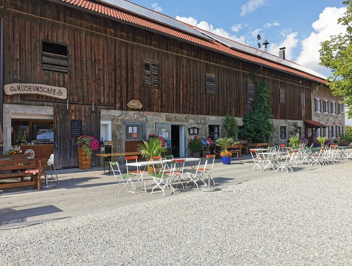 Museumcafe Vor einem alten Haus stehen viele Tische. Bunte Blumen schmücken den Platz. Gäste sitzen draußen.