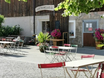 Museumcafe Tische und Stühle stehen vor dem Museumscafé. Bunte Blumen schmücken den Eingang.