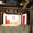 Pferdestall_innen_HD_16zu9.jpg Bühnenraum im Pferdestall mit Holzbalken, Stuhlreihen und Bühne mit rotem Vorhang und Scheinwerfern.