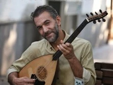 Mann spielt Saiteninstrument an einem Tisch, über ihm steht der Schriftzug Mehmet Atli