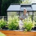 Judith Rakers Judith Rakers gießt grüne Gemüsepflanzen in einem Hochbeet vor einem modernen Gewächshaus.