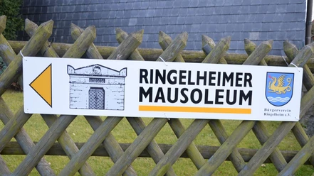 Mausoleum_Ringelheim_HD_16zu9.JPG Hinweisschild zum Ringelheimer Mausoleum mit Pfeil, Gebäudeskizze und Wappen an Holzzaun befestigt