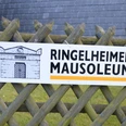 Mausoleum_Ringelheim_HD_16zu9.JPG Hinweisschild zum Ringelheimer Mausoleum mit Pfeil, Gebäudeskizze und Wappen an Holzzaun befestigt