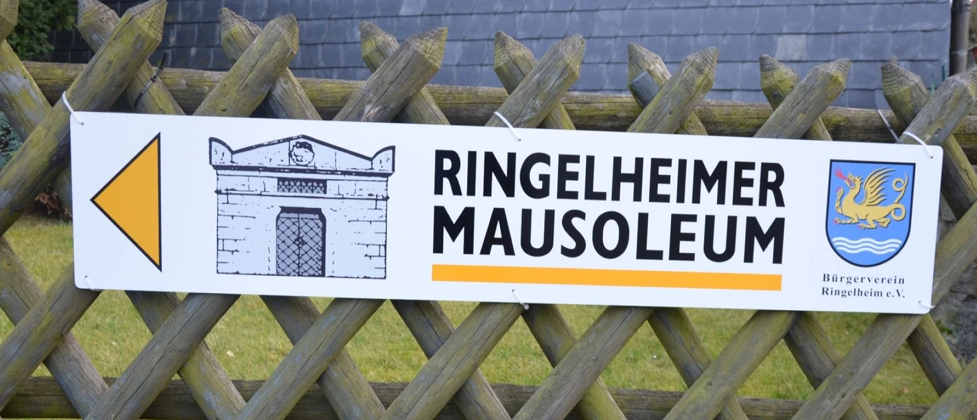 Mausoleum_Ringelheim_HD_16zu9.JPG Hinweisschild zum Ringelheimer Mausoleum mit Pfeil, Gebäudeskizze und Wappen an Holzzaun befestigt