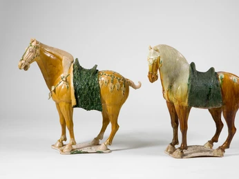Saddled horses, earthenware, three-color glaze (sancai), China, Tang dynasty (618-907). Zwei glasierten Pferdeskulpturen mit reich verzierten Sätteln auf hellem HintergrundTwo glazed horse sculptures with richly decorated saddles on a light background
