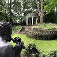 Thieles Garten (c) Mailin Knoke (30).JPG Steinfigur mit Flöte "Pan blickt auf die Sonennanbeterin" vor einem kleinen Teich und Pavillon im bewaldeten Thieles Garten in Bremerhaven