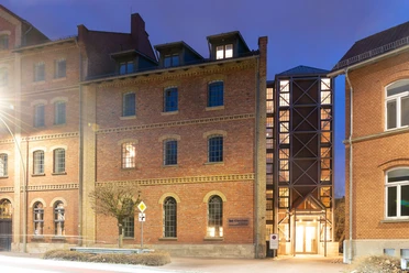 WF-Bundesakademie-Gästehaus.jpg Backsteingebäude mit vielen Fenstern. Heller Eingang mit Glasfront bei Abendlicht
