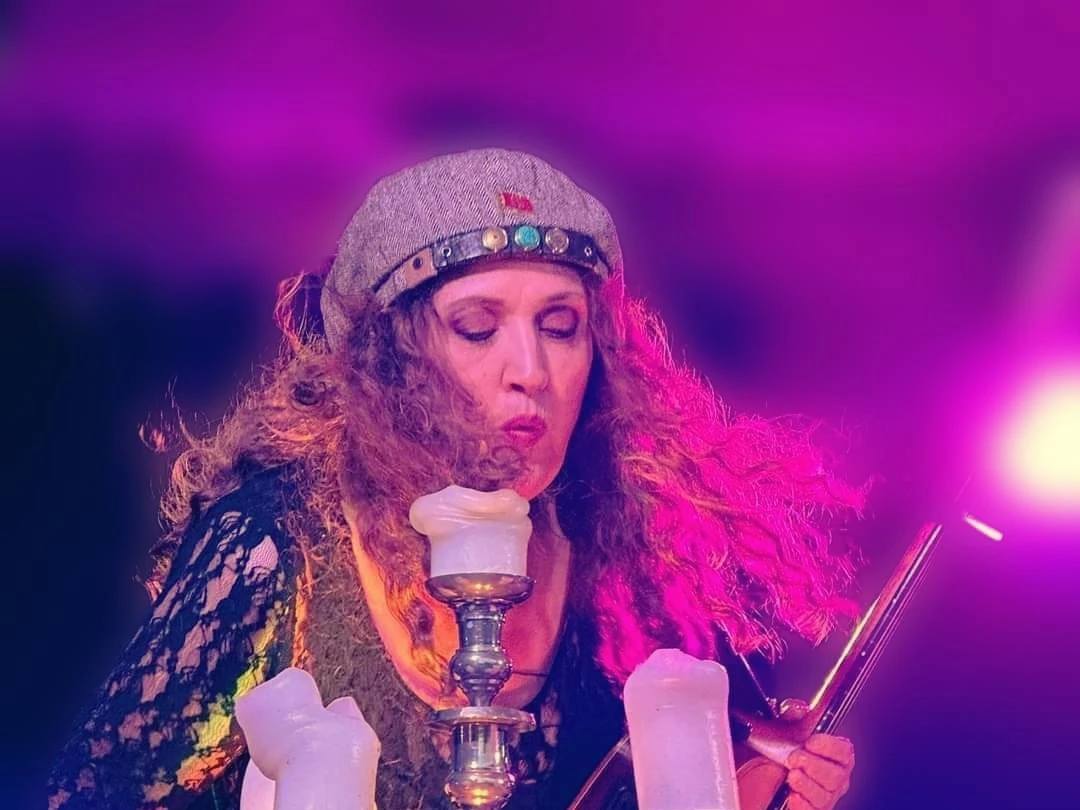 Pressefoto von Jan Rüther Musikerin mit Gitarre und grauer Mütze spielt auf der Bühne im violetten Licht hinter einem Kerzenständer.