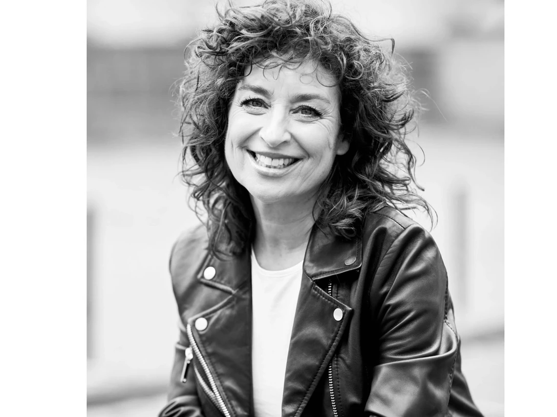 Profilbild von Isabel Varell Frau mit lockigen Haaren und Lederjacke lächelt in die Kamera, Porträtaufnahme in Schwarz-Weiß