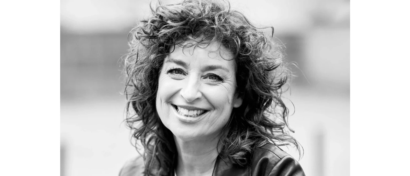 Profilbild von Isabel Varell Frau mit lockigen Haaren und Lederjacke lächelt in die Kamera, Porträtaufnahme in Schwarz-Weiß