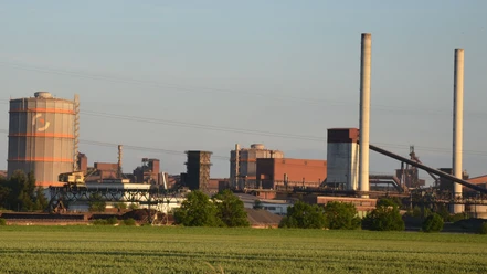Huettenwerk_Salzgitter_HD_16zu9.JPG Blick auf das Hüttenwerk Salzgitter mit Industrieanlagen, Türmen und Leitungen hinter grünen Feldern.