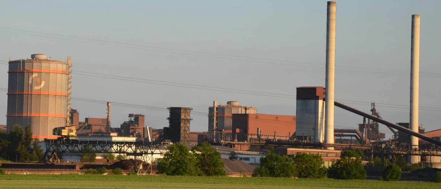 Huettenwerk_Salzgitter_HD_16zu9.JPG Blick auf das Hüttenwerk Salzgitter mit Industrieanlagen, Türmen und Leitungen hinter grünen Feldern.