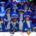 Kinderkarneval 2026.2png.png Kinder tanzen auf einer Bühne. Sie tragen blaue Kostüme mit weißen Hüten.