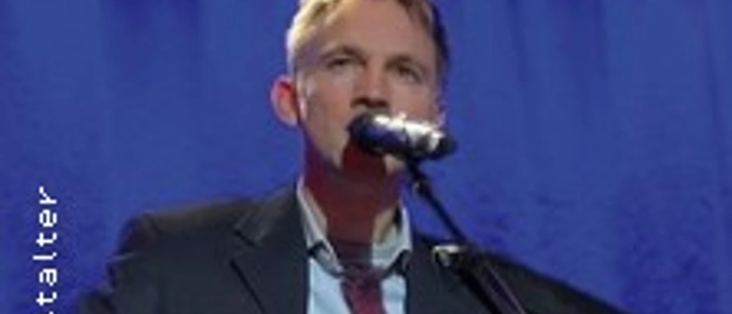 Ein Mann im Anzug steht vor blauem Vorhang und singt in ein Mikrofon.