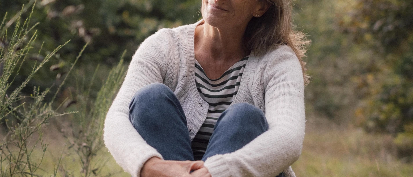 Auf dem Bild ist die Gästeführerin Claudia Krone zu sehen. Sie sitzt auf einem Baumstamm - im Hintergrund die Natur.