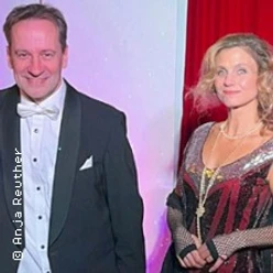 Mann im Smoking und Frau im 20er-Jahre-Kleid vor rotem Vorhang.