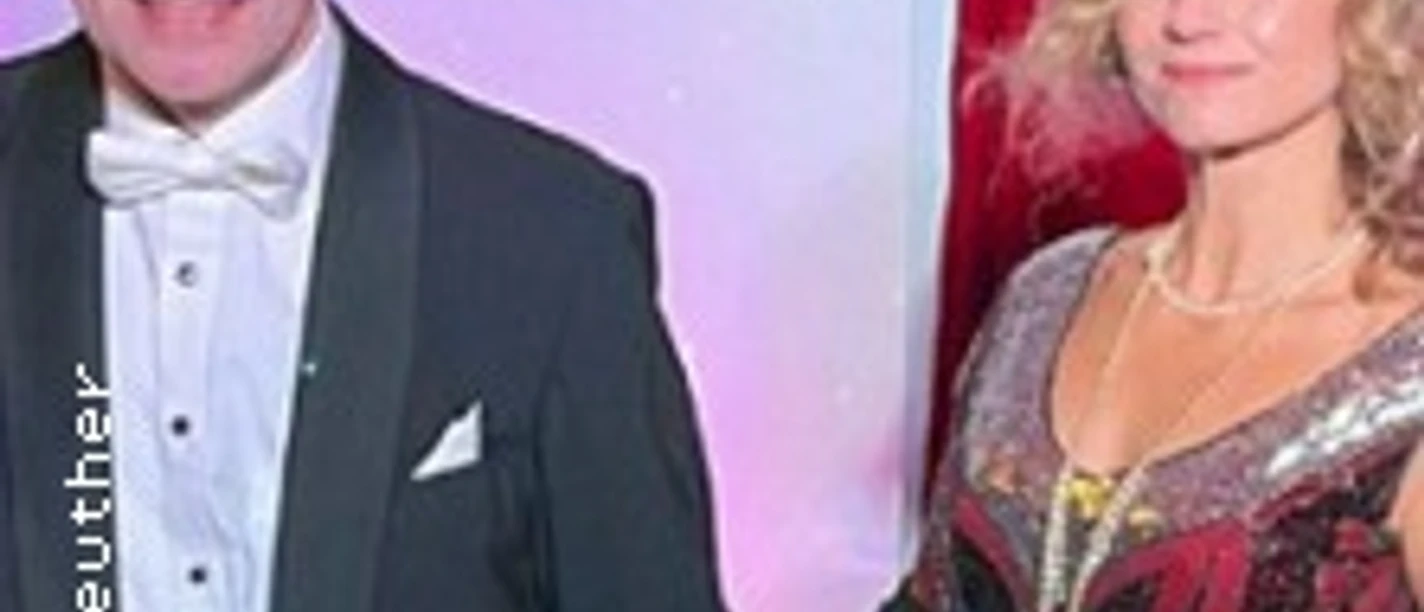 Mann im Smoking und Frau im 20er-Jahre-Kleid vor rotem Vorhang.