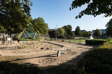 Spielplatz am Holzhafen Bremerhaven mit Klettergerüst, Wippe und Blick auf Teich und Springbrunnen im Park