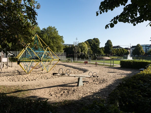 Spielplatz Holzhafen Q5617 (c) Helmut Gross_Erlebnis Bremerhaven.jpg Spielplatz am Holzhafen Bremerhaven mit Klettergerüst, Wippe und Blick auf Teich und Springbrunnen im Park