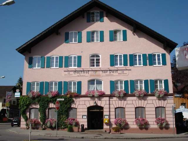 Gasthof zur Post.jpg Großes rosa Haus mit Blumen an Fenstern. Blaue Läden geben freundliche Wirkung.