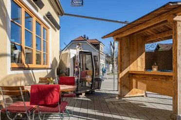 Gasthof Sonne Sonniger Außenplatz mit Tischen, roten Stühlen und einer alten Gondel am Weg.